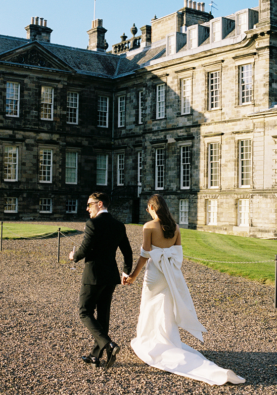 Bride and groom walking away holding hands on grounds